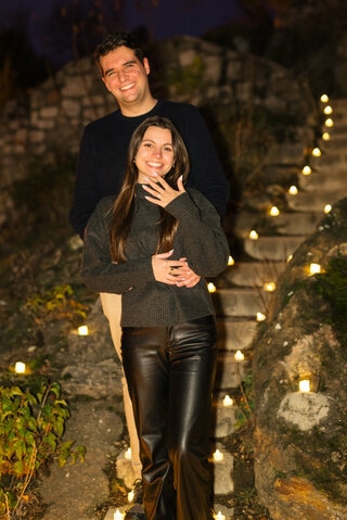 A happy couple celebrating their engagement proposal on the Gellért Hill in Budapest, standing on a romantically lit stone staircase surrounded by candles